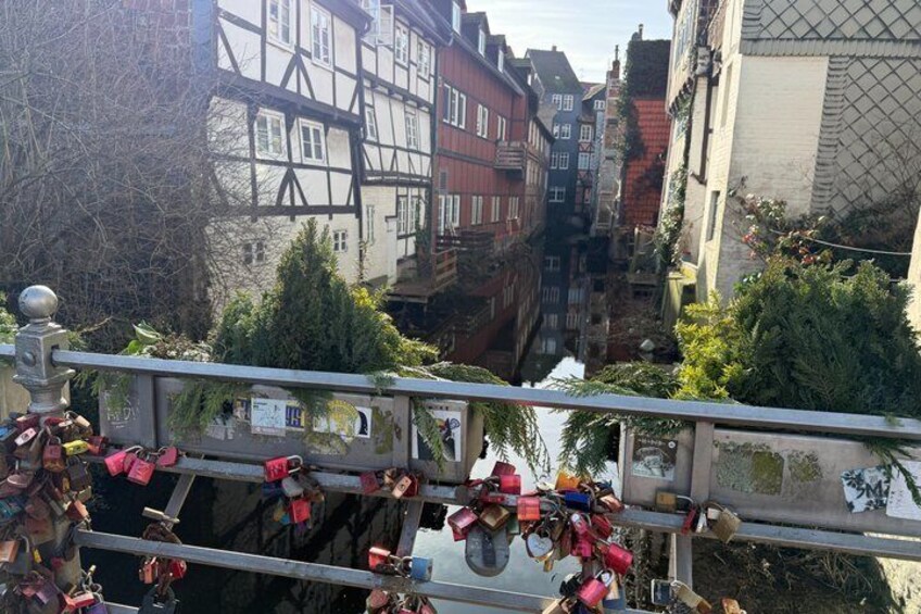 A narrow waterway flanked by traditional half-timbered buildings, a bridge with locks, and greenery. 4