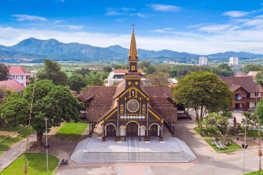 A church with a tall spire, surrounded by trees and buildings, with mountains in the background. 3