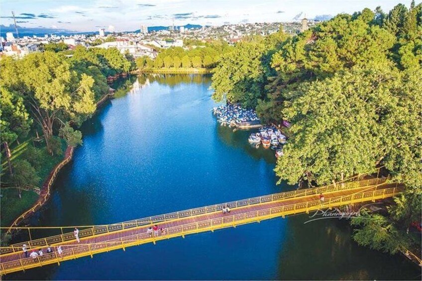 A suspension bridge over a river, surrounded by dense greenery and a distant cityscape. 2