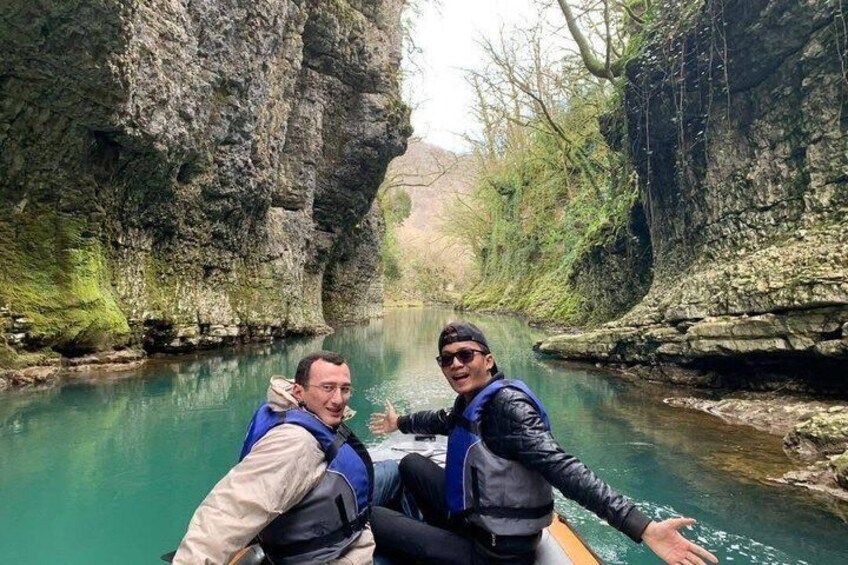 Two people in a boat on a river surrounded by rocky cliffs. 1