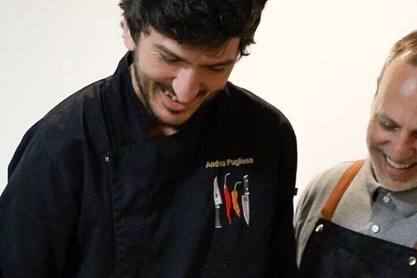 Two people in a kitchen, one wearing a black chef's jacket with a name and tools embroidered on it. 5