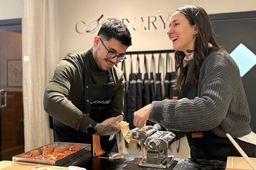 Two people preparing food, with a camera and a tray of pastries on the table. 1