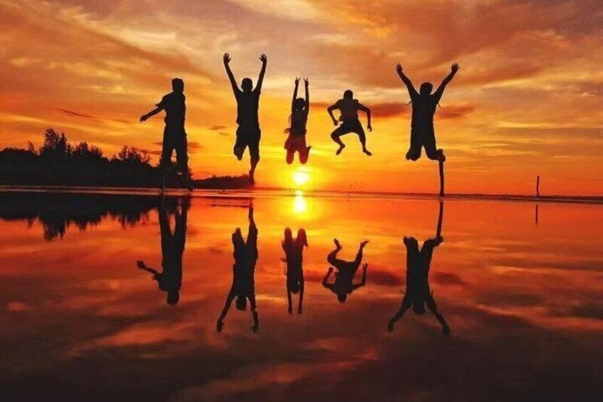 Silhouettes of people jumping against a sunset over a calm body of water. 1