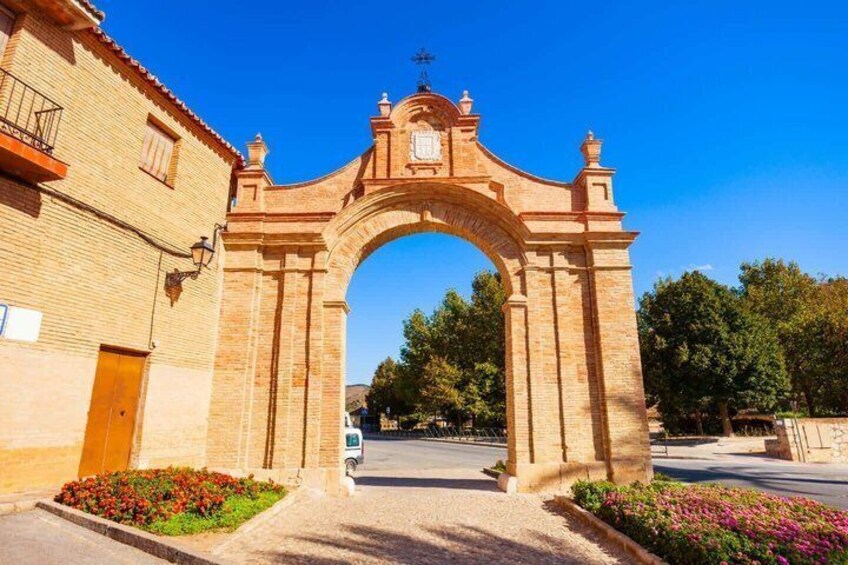 A stone archway with a cross at the top, surrounded by greenery and a clear blue sky. 5