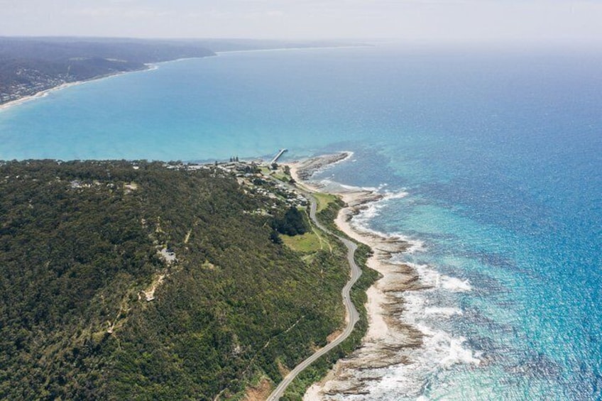 A coastal landscape with a winding road, dense forest, and a clear blue sea. 4