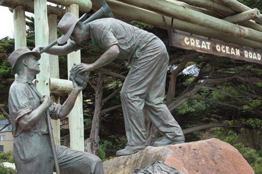 A statue of two men working, with a sign reading 'GREAT OCEAN ROAD' in the background. 2