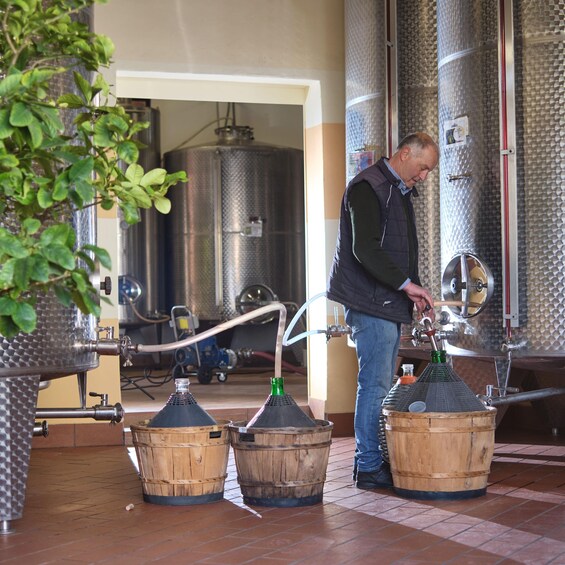 A person operating a brewing apparatus with wooden barrels and stainless steel tanks in a brewery. 2