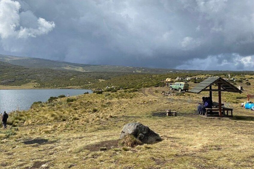 A grassy landscape with a lake, a wooden shelter, and a vehicle. 5