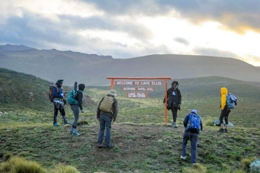 A group of hikers at a mountain trailhead with a sign reading 'WELCOME TO LAKE ELLIS.' 3