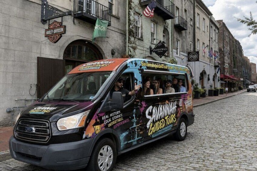 A tour bus with 'Savannah Guided Tours' branding parked on a cobblestone street. 2