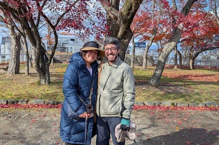 Two people standing in a park with autumn-colored trees. 1