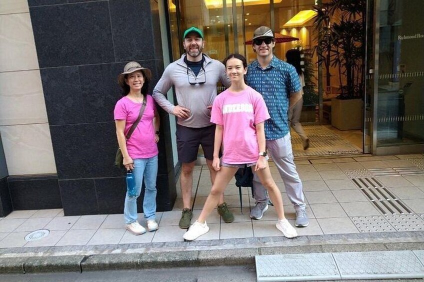 A group of people standing on a sidewalk in front of a building with a glass entrance. 2