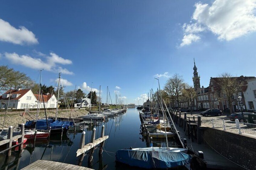 A calm canal with boats docked, a bridge, and buildings along the water. 1