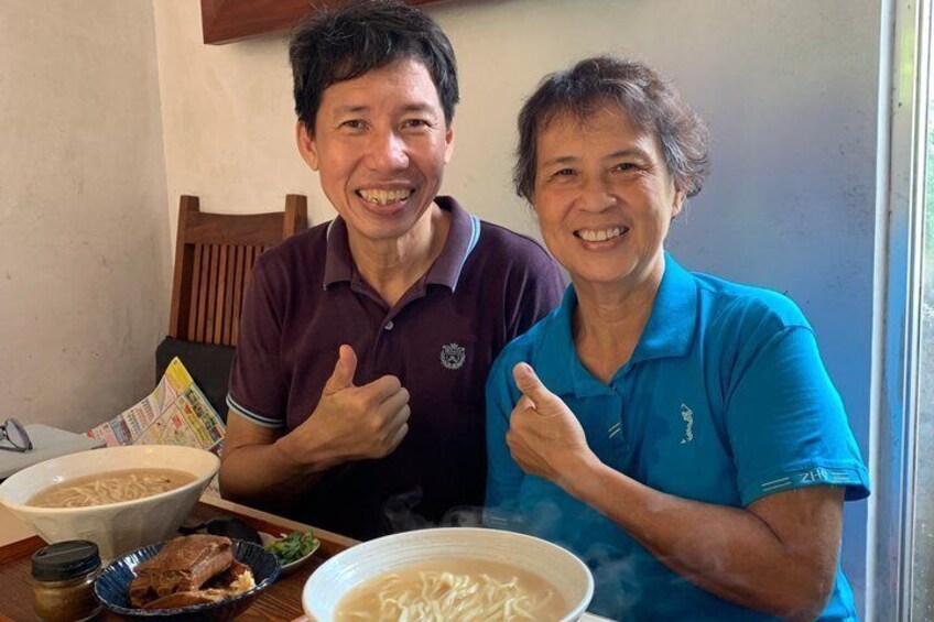 Two people sitting at a table with bowls of food, including noodles and a bowl of soup. 4