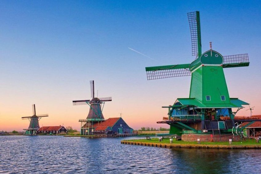 Three windmills by a calm river at sunset. 1