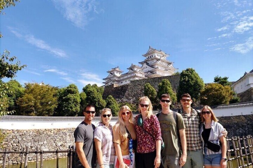 A group of people standing in front of a castle with multiple tiers and white walls. 1