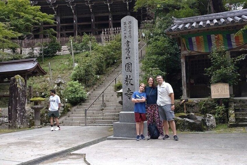 A stone monument with Japanese characters, a staircase, and traditional Japanese architecture. 2