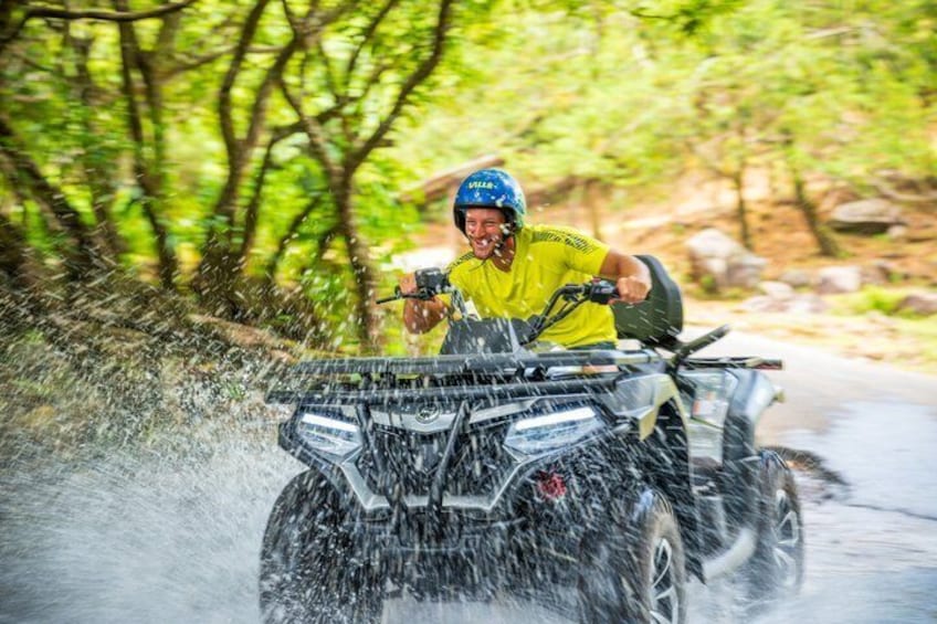 A person riding a quad bike through a forested area with trees and a road. 2