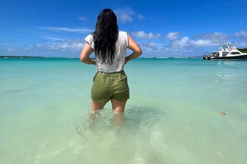 A person standing in shallow water with a boat in the background. 3