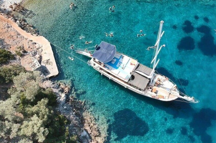 A sailboat anchored near a rocky shoreline with clear turquoise water. 1