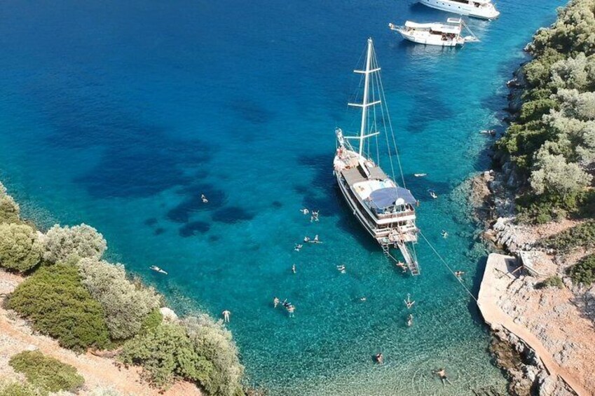 A clear blue sea with a sailboat anchored near the shore, surrounded by rocky coastline and sparse vegetation. 3
