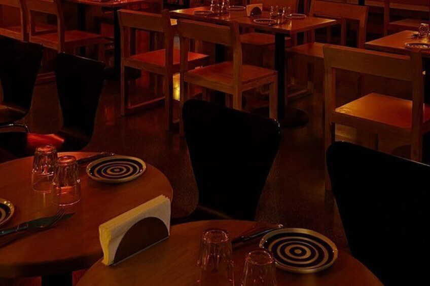 A dimly lit restaurant with wooden tables and chairs, some with plates and cutlery. 2