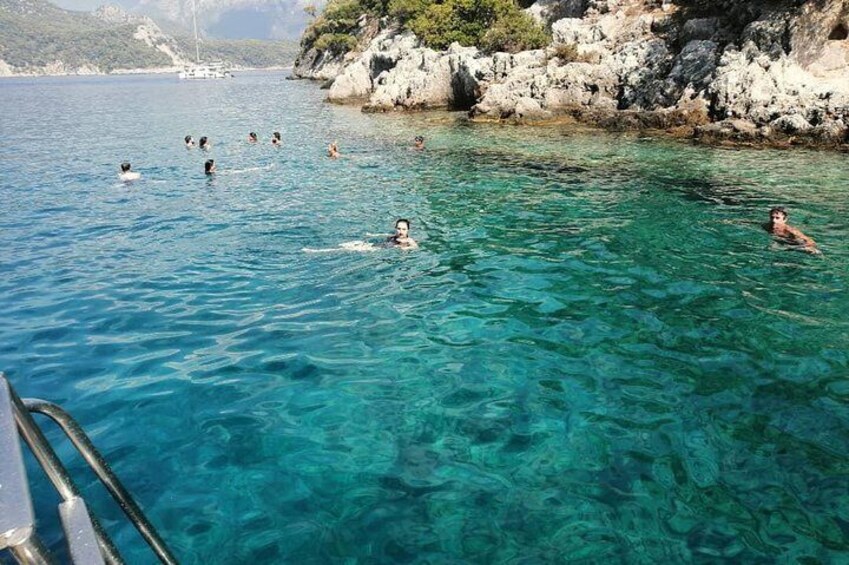 People swimming in clear blue water with rocky cliffs in the background. 2