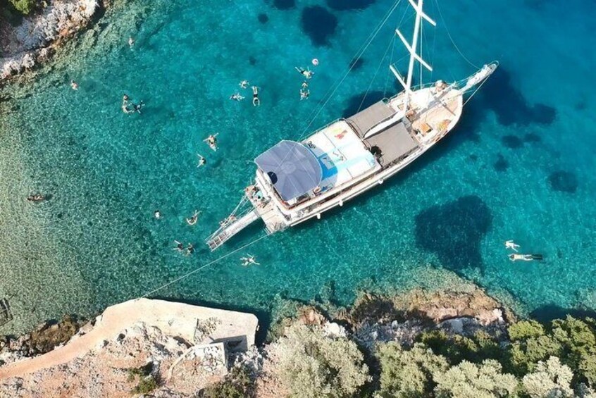 A sailboat anchored in clear turquoise waters with people swimming and sunbathing nearby. 1