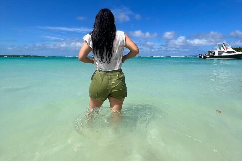 A person standing in shallow water with a boat in the background. 1