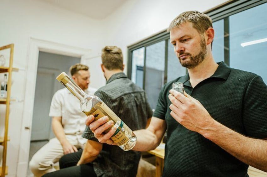 A person holding a bottle and a glass, with another person in the background. 4