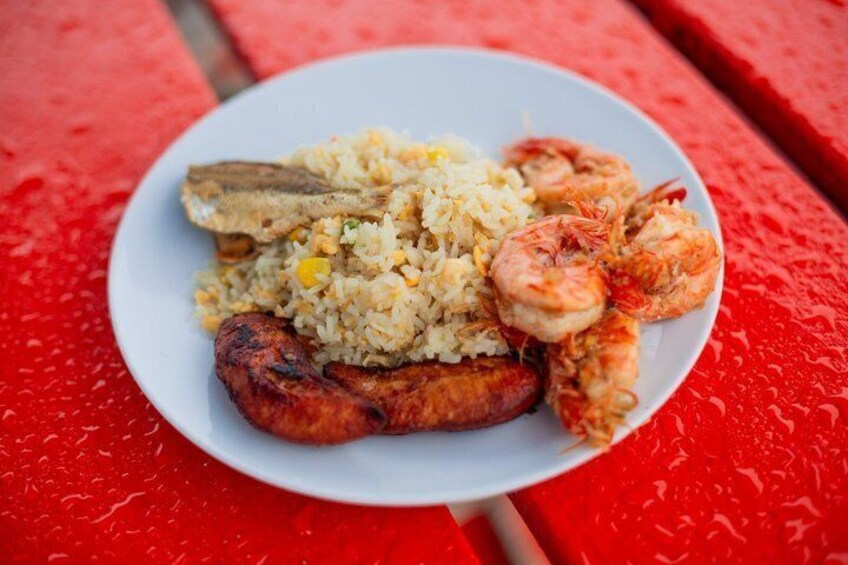 A plate of fried rice, shrimp, and a grilled sausage on a red table. 3