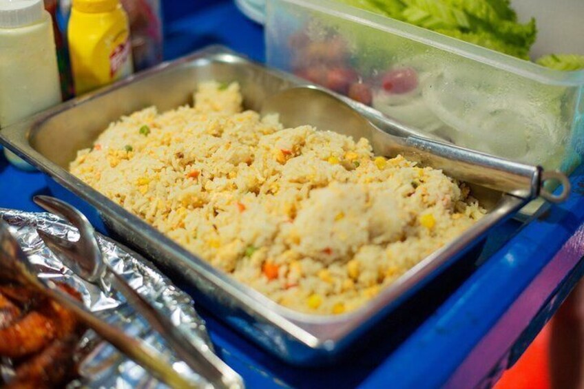 A tray of fried rice with vegetables, a container of salad, and condiments on a table. 4