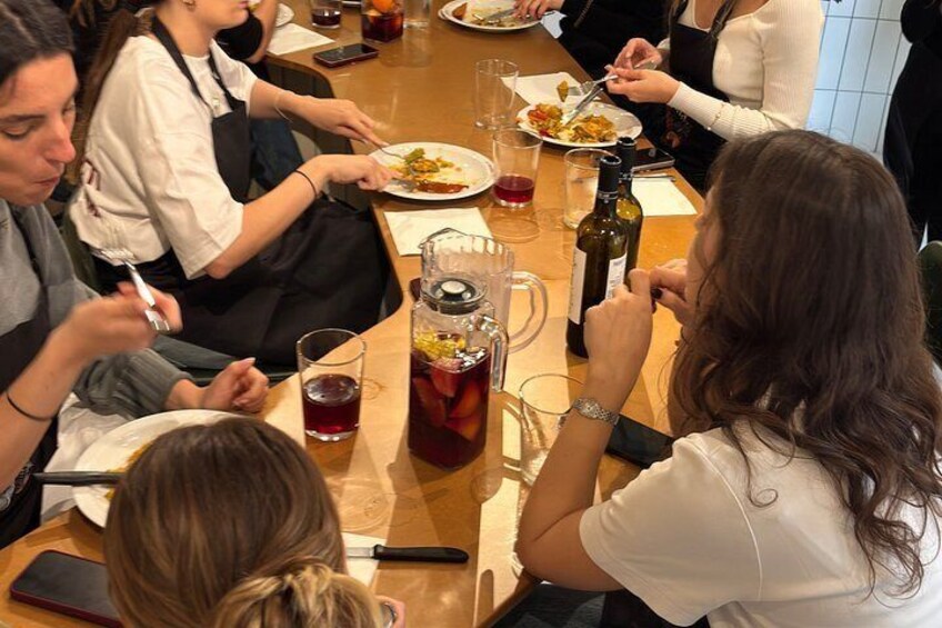 A group of people dining at a table with plates of food, glasses of beverages, and a bottle of wine. 4