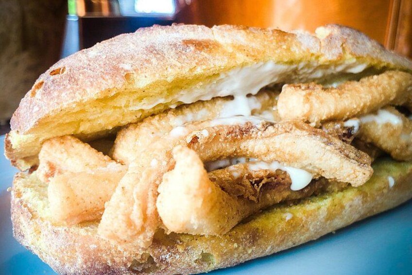 A sandwich with a crusty bread exterior, fried fish fillets, and a creamy sauce. 2