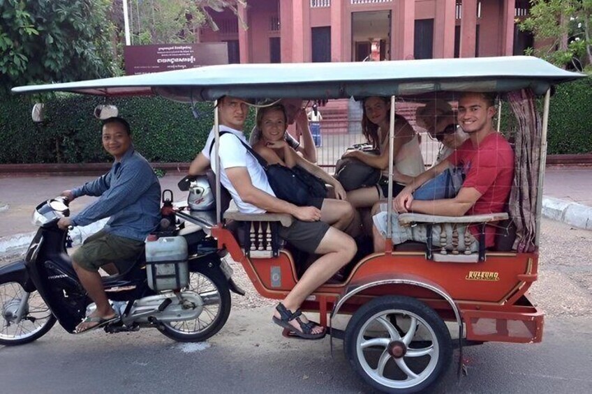 A group of people on a three-wheeled vehicle with a canopy, parked on a street. 3
