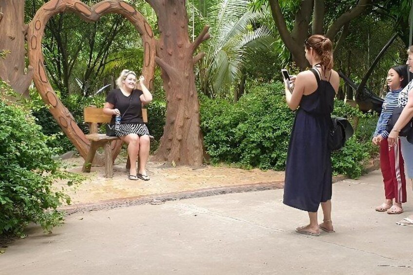 A woman taking a photo with her phone, a heart-shaped bench, and a tree in the background. 2