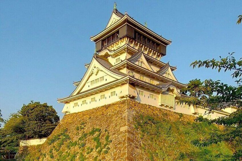 A traditional Japanese castle with multiple tiers, surrounded by greenery and a clear sky. 1