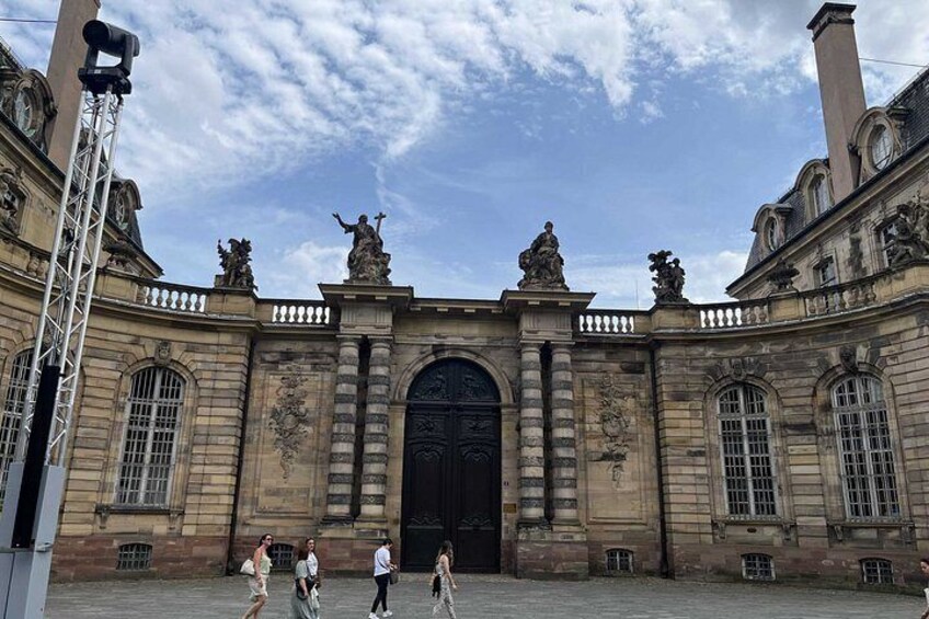 A historic building with large arched windows and statues on the roof. 2