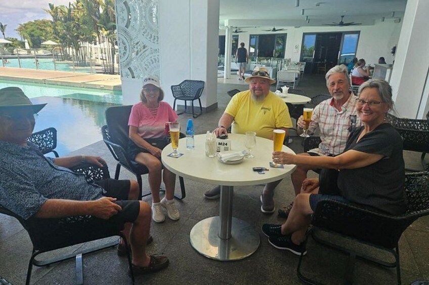 A group of people seated around a round table with drinks, overlooking a pool area. 4