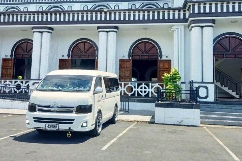 A white van parked in front of a building with classical architecture, including columns and arched doorways. 2