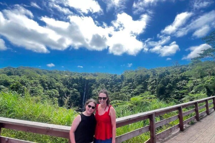 Two people standing on a wooden bridge with a forested landscape in the background. 3