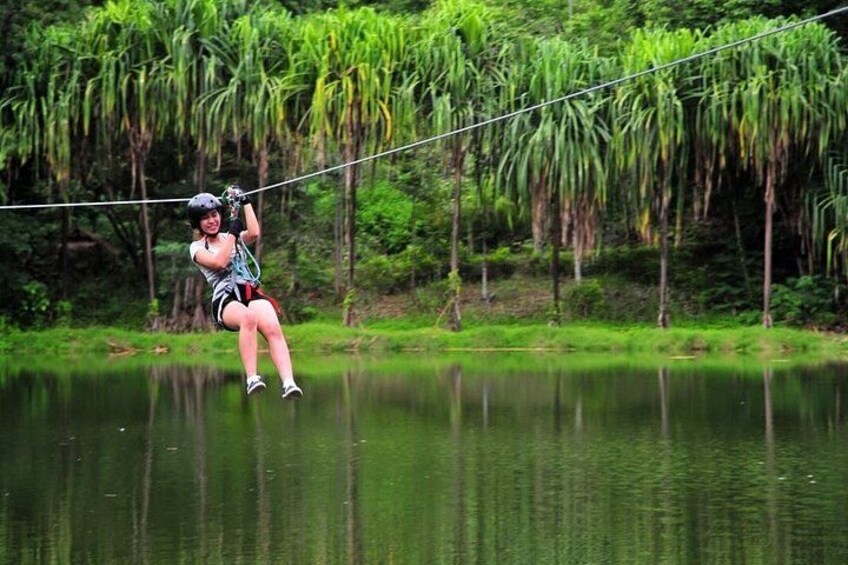 A person zip-lining over a body of water with dense greenery in the background. 1