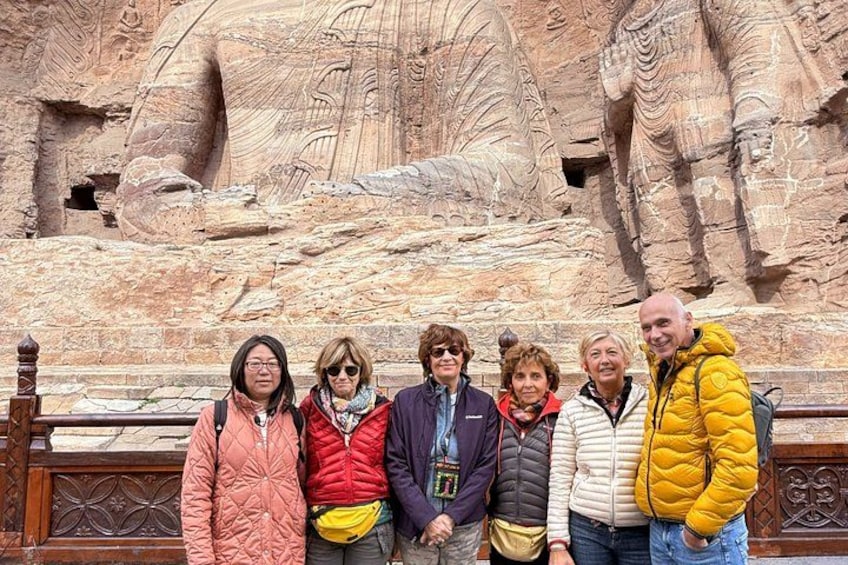 A group of people standing in front of a large rock carving. 1