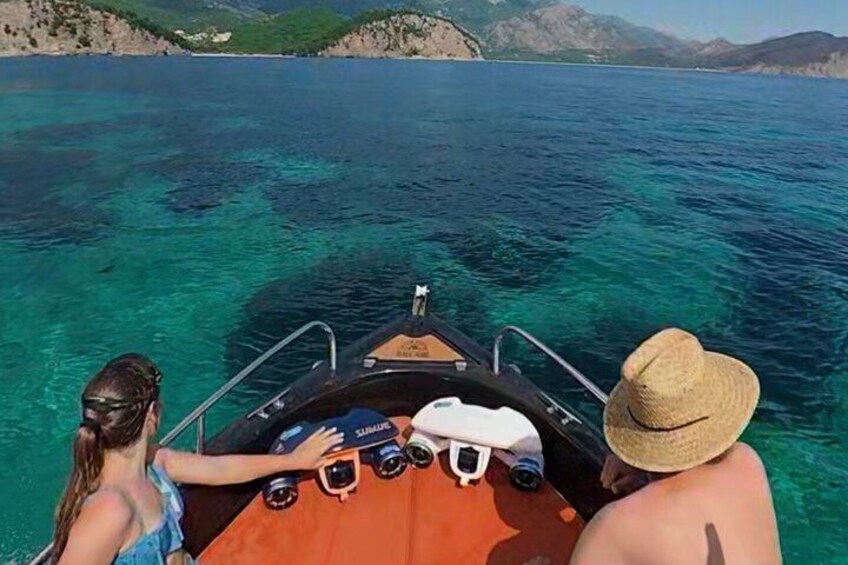 A boat on clear turquoise water with a person in a straw hat and another in a blue swimsuit. 1