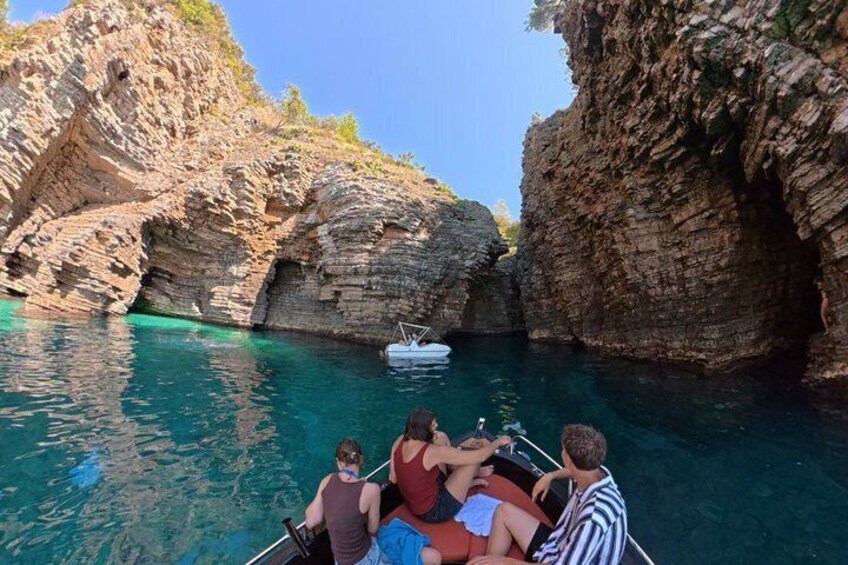A boat with people on a clear turquoise sea, surrounded by rocky cliffs. 2