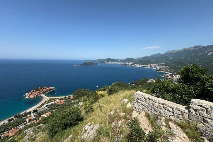 A coastal landscape with a stone wall, a beach, and a distant town. 5
