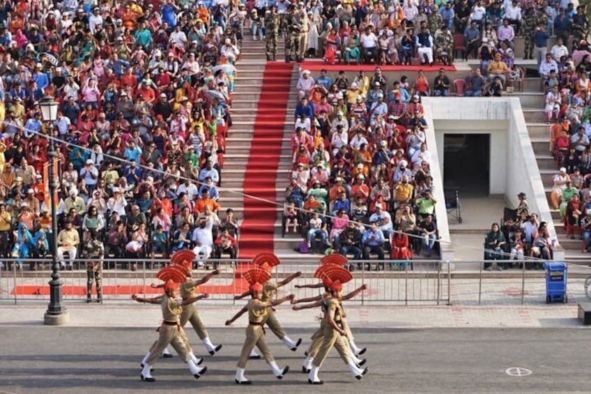A group of performers in golden costumes with red fans, walking on a stage in front of a large, seated audience. 4