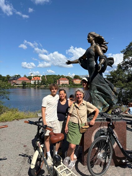 A group of people posing with a statue of a woman by a lake with buildings in the background. 4