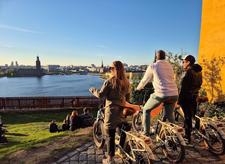 A group of people on bicycles overlooking a river with a cityscape in the background. 1