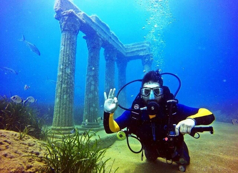 A diver underwater near ancient ruins with columns, surrounded by marine life. 1